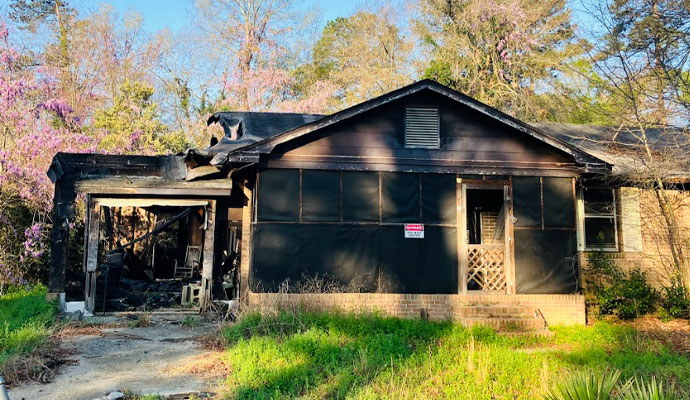 Severely Fire-Damaged House Exterior Front view of a house with severe fire damage, showing charred walls, and a collapsed section