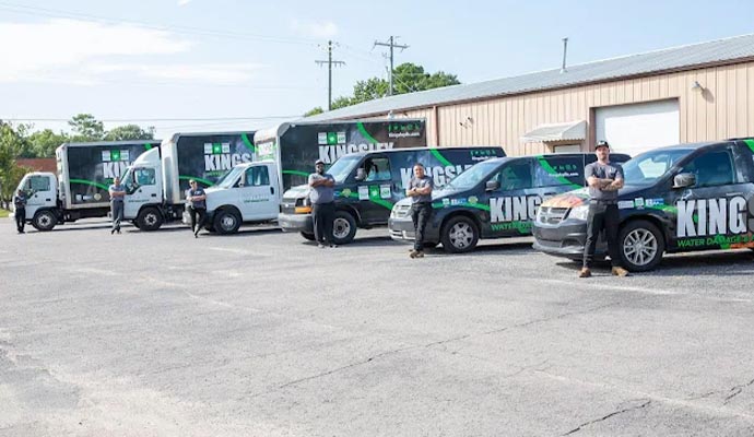 A line of professional water damage restoration trucks and vans from Kingsley with technicians standing in front of their vehicles in a parking lot