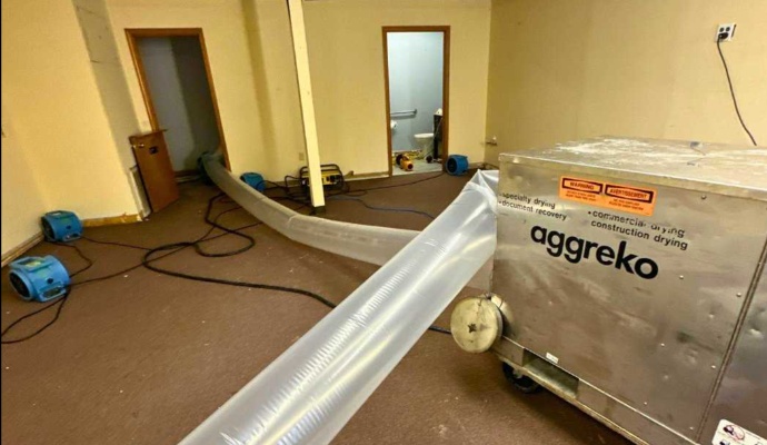 Large dehumidifiers system with plastic ducting and multiple air movers working to dry pooled water on carpeted floor
