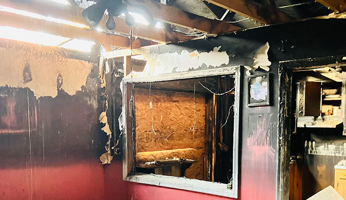 Interior Room with Extensive Fire Damage Interior room heavily damaged by fire, showing charred walls, exposed ceiling beams, peeled paint, and a burnt window.