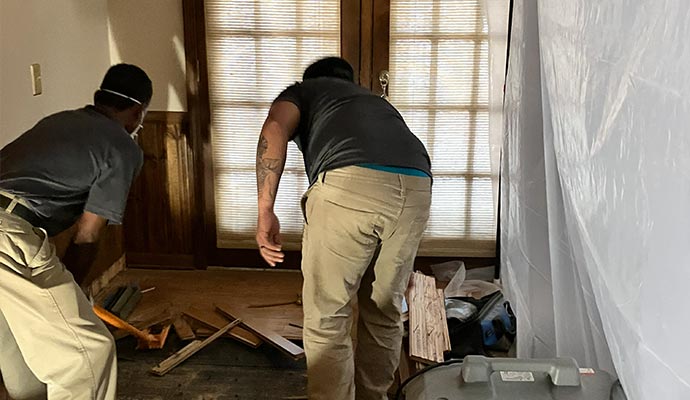 Two restoration technicians working in a room to dismantle and remove warped wood planks from a water-damaged floor