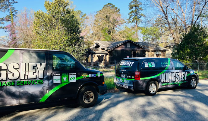 Restoration Service Vans at Fire-Damaged Home Two Kingsley restoration service vans parked on the street in front of a fire-damaged house.