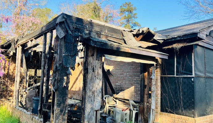 Severe Fire Damage to Home Structure A house with severe fire damage, showing charred wooden beams, collapsed roof sections, and burnt debris.