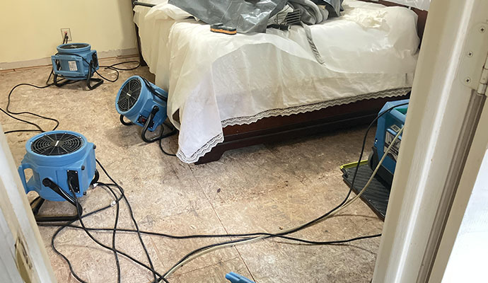 Industrial air movers and drying equipment placed around a bedroom to dry the floor.