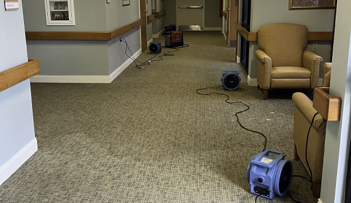 Air movers and drying fans placed along hallway carpet after water damage
